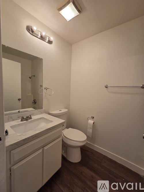 A bathroom with a toilet, sink, mirror, and towel rack.