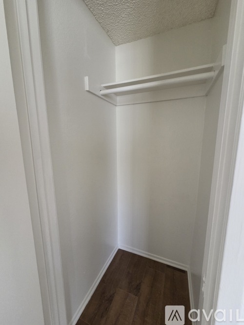 A small white closet with a shelf and wooden floors.