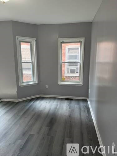 A room with grey walls and wooden flooring with two windows.