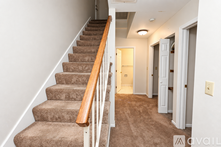 A staircase with a wooden handrail and beige carpeted steps leads to a hallway.