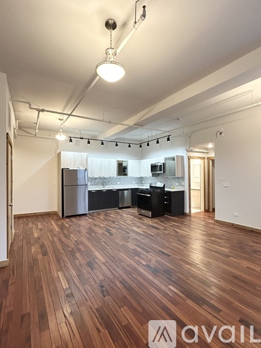 A room with wooden floors and a kitchen area in the background.