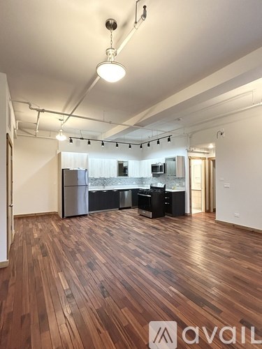 A room with wooden floors and a kitchen area in the background.