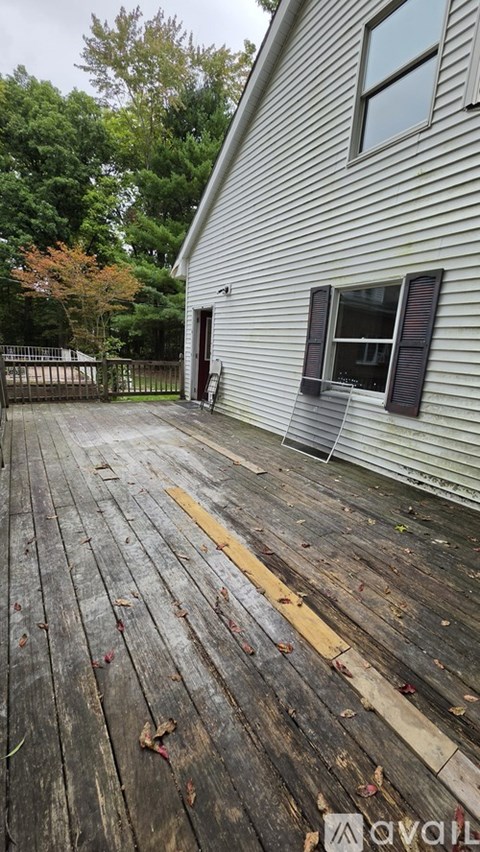 A wooden deck with a white house and trees in the background.