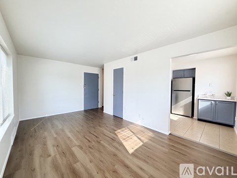 A spacious room with wooden flooring and a kitchen area with a refrigerator, oven, and microwave.