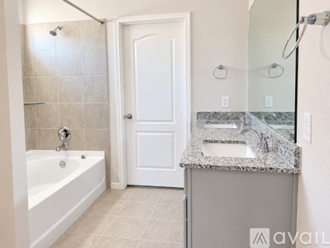 A bathroom with a white door, a bathtub, and a granite countertop.