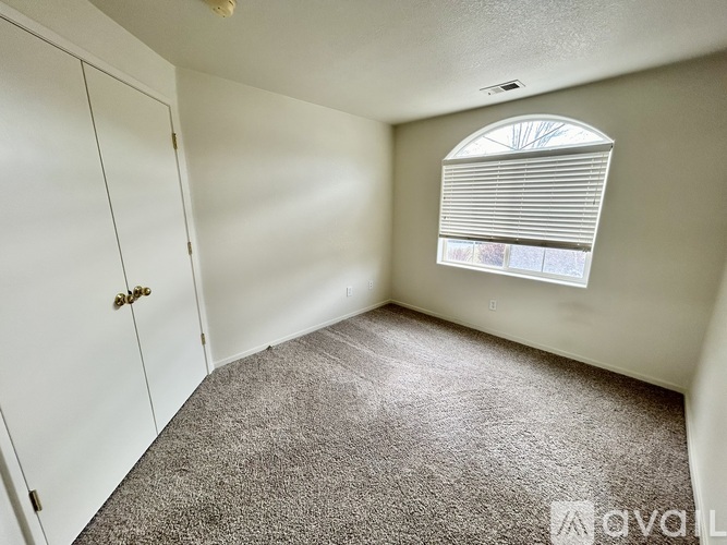 A room with a carpeted floor, a window with blinds, and a white door.