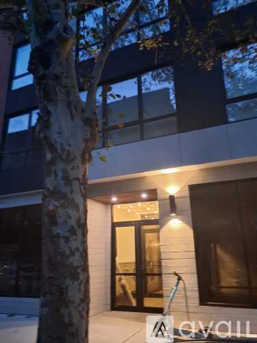 A tree stands in front of a building with a lit up entrance.