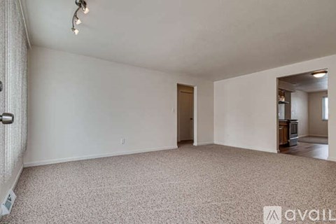 A spacious empty room with a carpeted floor and a door leading to another room.