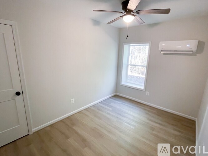 A room with a ceiling fan and a window with an air conditioner unit on the wall.