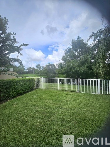 A well-maintained lawn with a white fence and trees in the background.