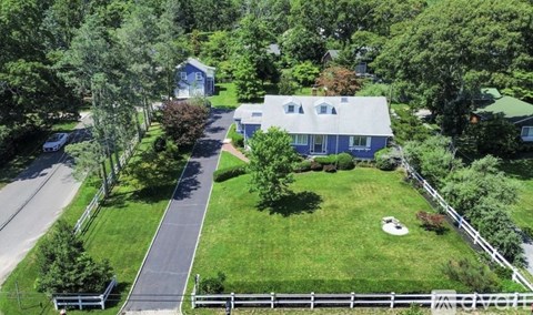 A house with a blue roof is surrounded by a white fence and green trees.