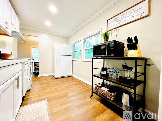 A kitchen with white cabinets and a black shelf with a microwave on top.