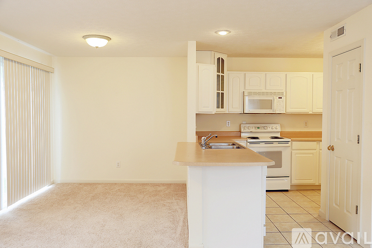 A kitchen with white cabinets and appliances, a sink, and a door leading to another room.