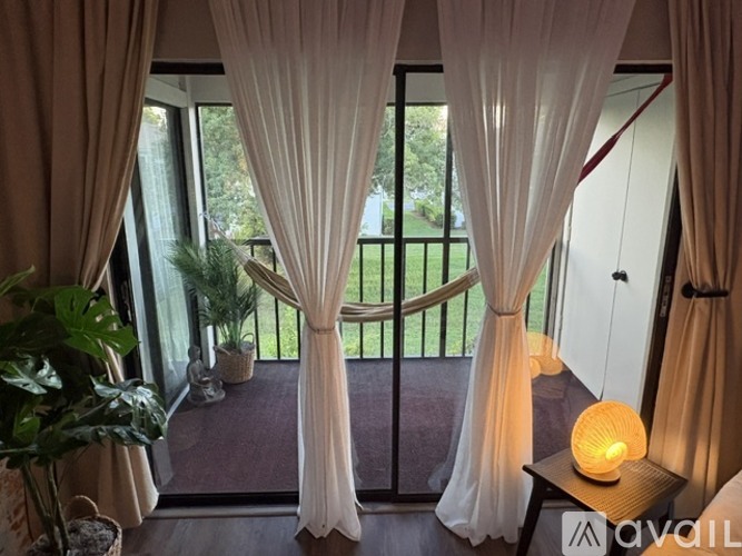 A balcony with a view of a green lawn and trees, with a table holding a lit candle.