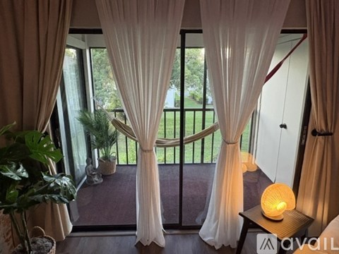 A balcony with a view of a green lawn and trees, with a table holding a lit candle.