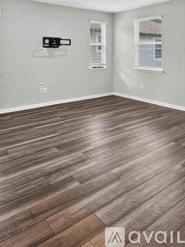 A room with wooden flooring and two windows.