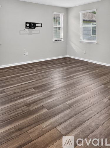 A room with wooden flooring and two windows.