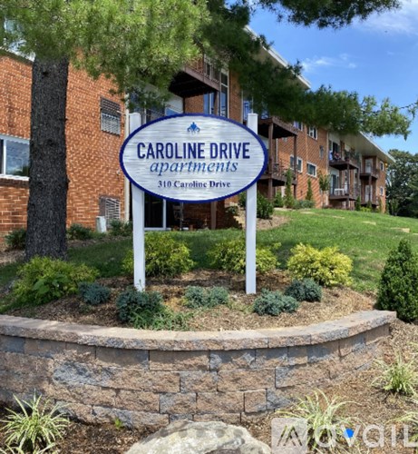 A sign for Caroline Drive Apartments stands in front of a brick building.