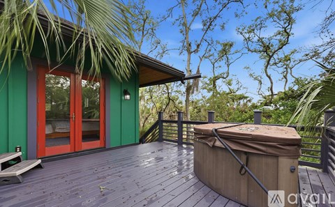 A hot tub sits on a wooden deck with a green building and trees in the background.