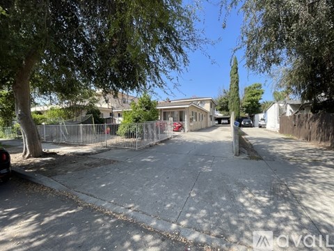A residential street with a house, trees, and a car parked on the side.