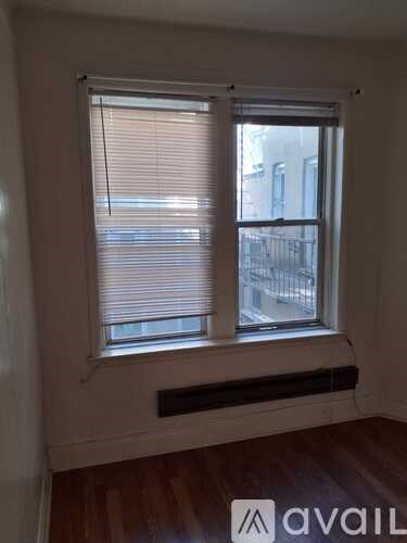 A window with blinds and a black frame in a room with wooden flooring.
