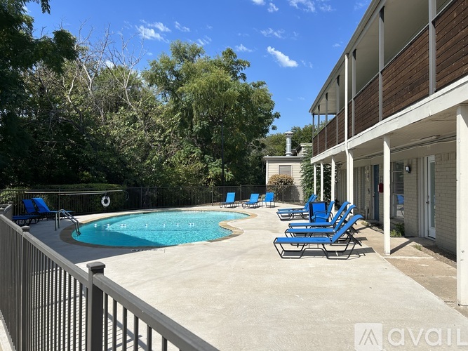 A pool surrounded by blue lounge chairs and a white fence.