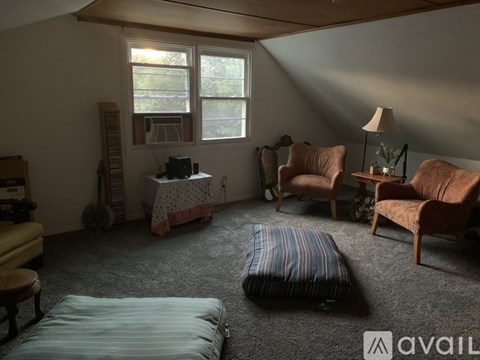 A living room with a sofa, two chairs, a bed, and a table with a lamp.