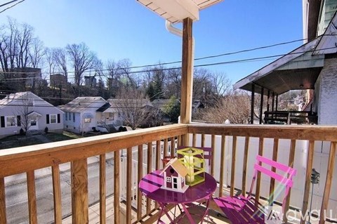 A small table with a pink chair and a doll house on it is on a balcony.