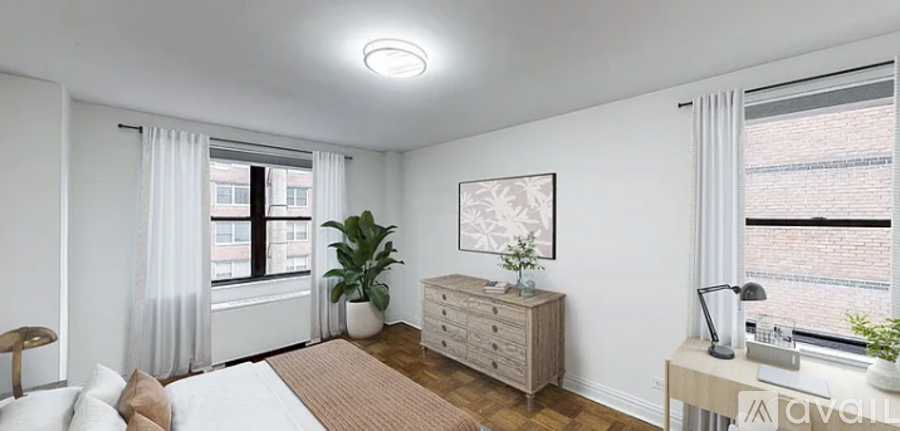 A well-lit bedroom with a large bed, a dresser, and a window with curtains.