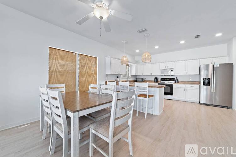 A kitchen with a table and chairs in the foreground and a refrigerator, oven, and cabinets in the background.