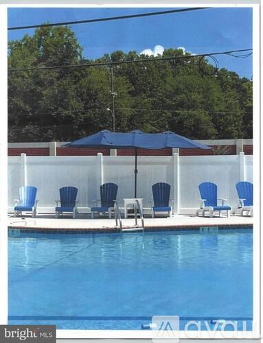 A pool with chairs and an umbrella is surrounded by a white fence.