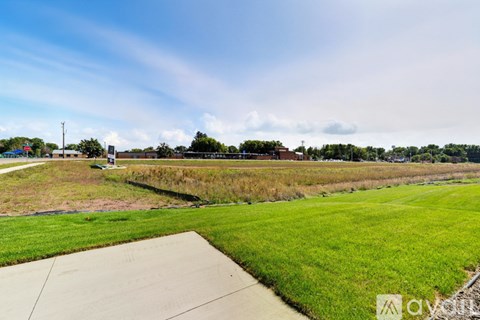 A grassy field with a concrete pathway in the foreground and a building in the distance.