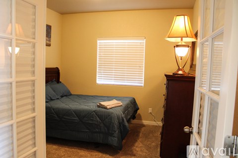 A bedroom with a bed, a nightstand with a lamp, and a window with blinds.