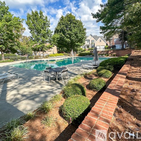 A pool surrounded by a brick border and greenery.