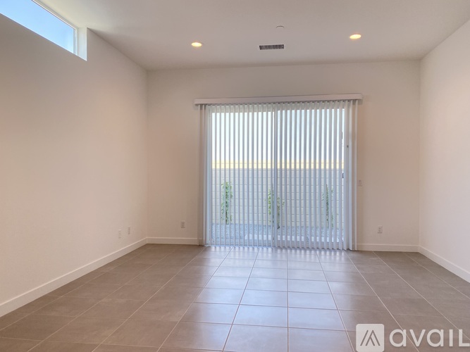 A spacious room with tiled flooring and a sliding glass door leading to a balcony.