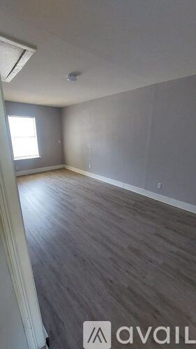 A room with wooden flooring and a window on the left side.