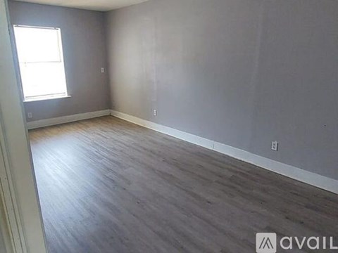 A room with wooden flooring and a window on the left side.