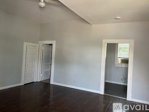 A room with wooden floors and white walls, with a door and a window.