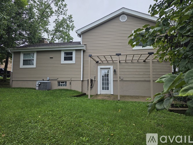 A house with a beige siding and a white door is surrounded by green grass.
