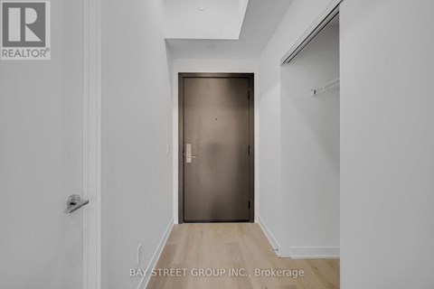 A white hallway with a wooden floor and a closed door.
