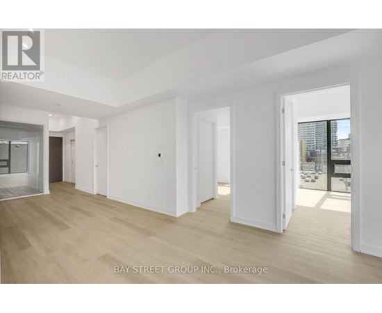 A spacious room with wooden flooring and white walls, with a view of a cityscape through a glass door.