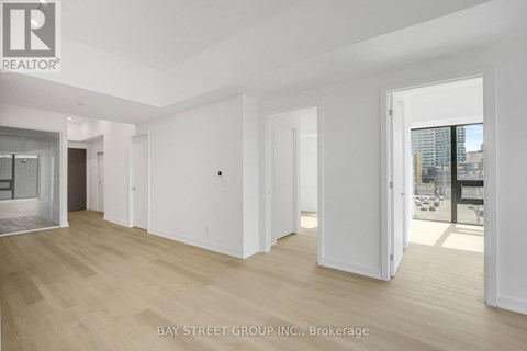 A spacious room with wooden flooring and white walls, with a view of a cityscape through a glass door.