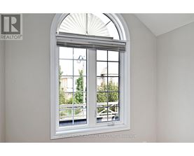 A white room with a large arched window that has a view of a balcony and trees.