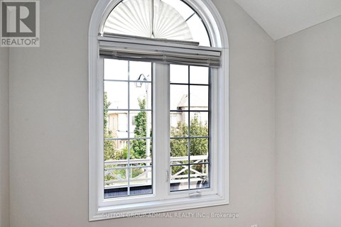 A white room with a large arched window that has a view of a balcony and trees.