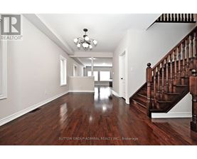 A spacious room with a wooden floor and a staircase on the right side.