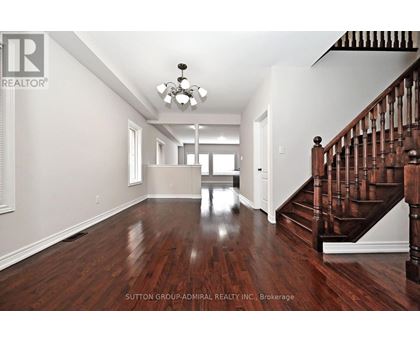 A spacious room with a wooden floor and a staircase on the right side.