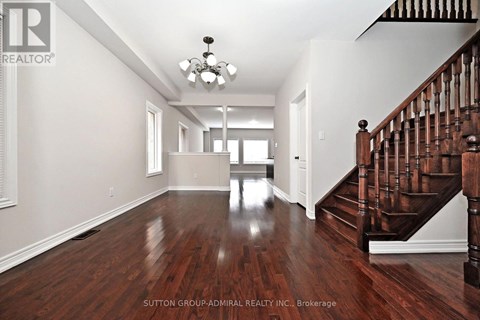 A spacious room with a wooden floor and a staircase on the right side.
