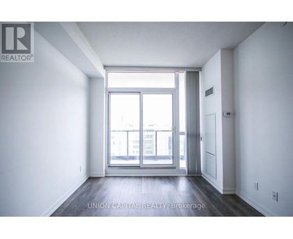 A spacious room with a large window and wooden flooring.
