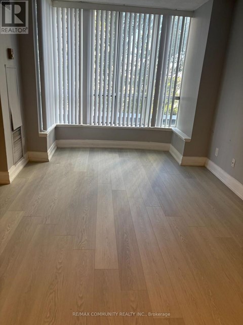 A room with a window covered in blinds and wooden flooring.