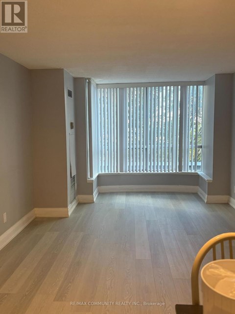 A room with light wood flooring and a window with blinds.